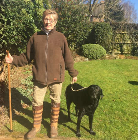 Linda, standing in her garden with a black labrador by her side.